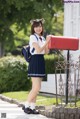 A woman in a school uniform holding a red mailbox.