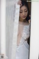 A woman in a white dress peeking out from behind a curtain.