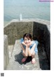 A little girl sitting on the edge of a concrete wall by the water.